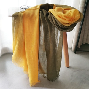 Detail of yellow and olive green cotton linen scarf with soft fringe on a wooden stool