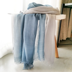 Close-up of blue-grey gradient cotton linen scarf with soft fringe on a white table