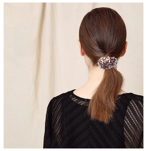 Detail of reversible sequin hair scrunchie in bronze and black on a low ponytail hair style