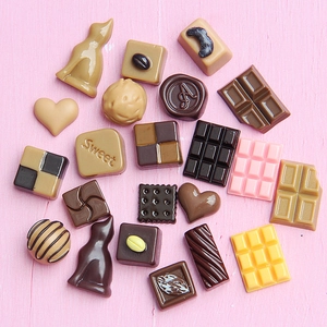 Miniature resin chocolate charms in various shapes on a pink wooden background