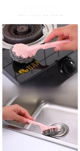 Detail of pink long-handled steel wool brush cleaning kitchen stove and sink surface