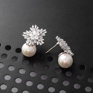 Detailed close-up of snowflake earrings featuring sparkling zircons and a white pearl drop