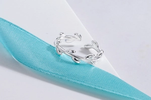 Detail shot of silver olive leaf open ring on white geometric stand with blue ribbon