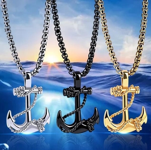 Trois colliers croix ancre nautique en argent, or et noir sur fond de mer au coucher du soleil