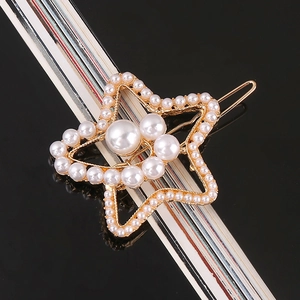 Detailed view of a star-shaped gold metal hair clip with inlaid pearls on a black background