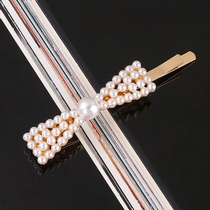 Detailed macro shot of a golden bow hair clip with white pearls on black surface