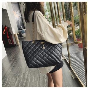Detail of black quilted shoulder bag with gold chain strap and deer charm on a model