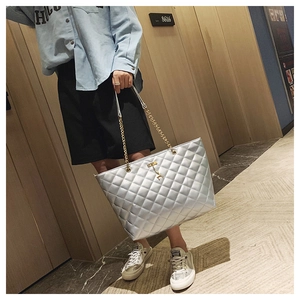 Close-up of silver quilted tote bag featuring a gold chain strap and deer charm detail