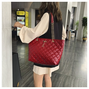 Close-up of red quilted tote bag with golden deer charm and chain straps on model