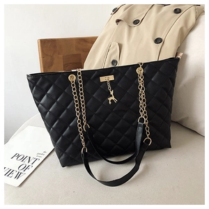 Detail of black quilted tote bag with golden deer pendant and elegant chain strap