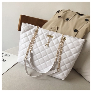 Detail of white quilted tote bag featuring gold chain strap and deer charm on sofa