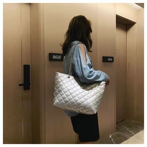 Close-up of a silver quilted tote bag with a gold chain strap on a model's shoulder