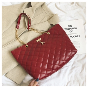 Detail of red quilted shoulder bag with gold chain and deer charm on white fabric