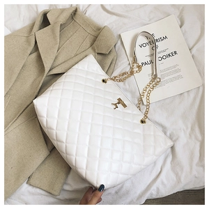 Close-up of white quilted tote bag featuring golden deer logo and chain strap detail