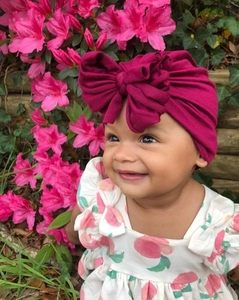 Primo piano di un bambino che indossa un turbante magenta con un grande fiocco in giardino