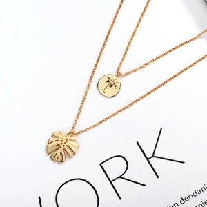 Detail of gold double-layered necklace with palm tree and monstera leaf pendants
