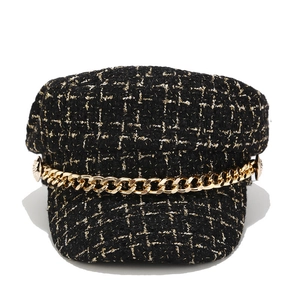 Detailaufnahme der schwarz-goldenen Tweed-Mütze mit dekorativer matter Goldkette