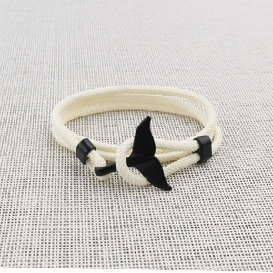 Detail of a beige woven bracelet featuring a black metal whale tail charm on fabric