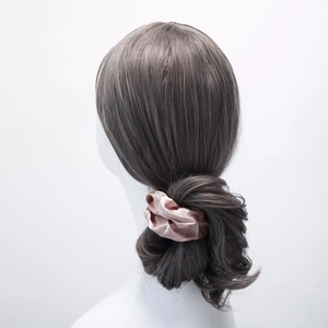 Detailed view of a soft pink satin scrunchie styled on a low bun hair arrangement