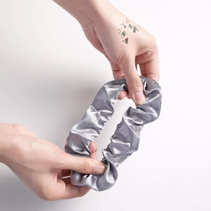 Detail of silver grey satin scrunchie being stretched to show high elasticity and texture