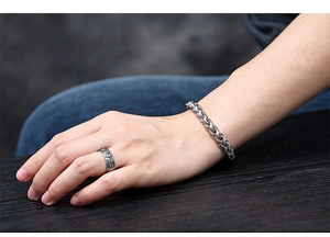 Close-up of a silver woven titanium steel bracelet and engraved ring on a person's wrist