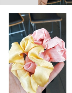 Detail shot of pleated satin scrunchies in yellow and pink with silk-like texture
