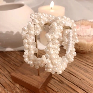 Detailed view of handmade white pearl beaded hoop earrings on a rustic wooden stand
