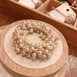 Elegant white pearl hair tie and bracelet set on a round wooden jewelry display stand