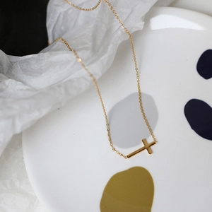 Detail of a minimalist 18K gold plated titanium steel necklace with a horizontal cross charm
