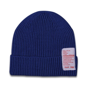 Detail of blue ribbed knit beanie featuring a white rectangular woven patch with red text