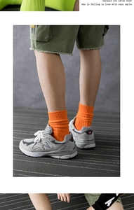 Close-up of bright orange ribbed crew socks styled with grey retro sneakers on a rug