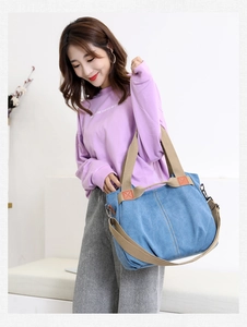 Detail of blue canvas shoulder bag featuring brown woven handles and metal hardware accents