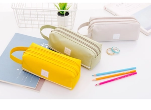 Detalle de estuches de lona amarillos, verdes y beige con cremalleras dobles y un asa