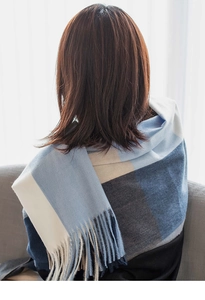 Detail of blue and beige plaid scarf with soft fringe tassels worn by a model