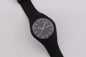 Detail of minimalist black Geneva watch with silicone strap and round dial on gray background