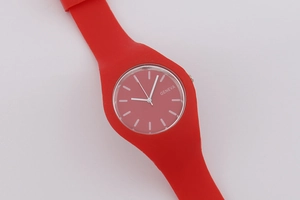 Close-up of a red silicone watch strap and Geneva dial on a soft gray background