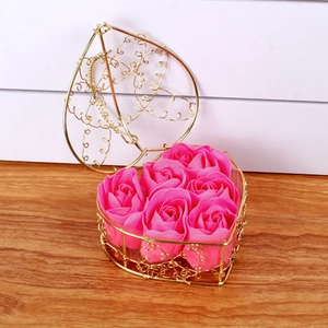 Close-up of six pink soap roses in a golden heart-shaped wire basket on wood