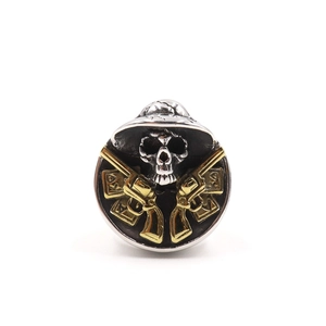 Detail of silver skull ring featuring dual golden guns and poker card gothic patterns