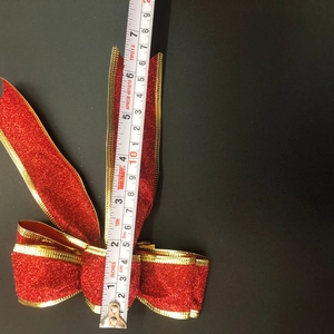 Close-up of red glitter Christmas bow with gold trim showing 18cm measurement scale