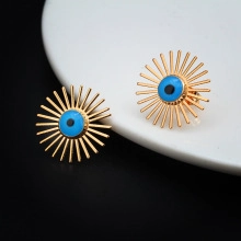 Macro shot of gold Evil Eye stud earrings with blue and black inlay on a white tray