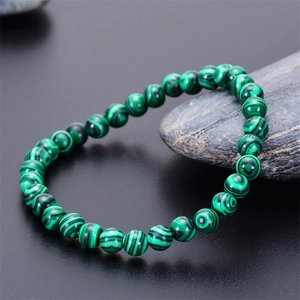 Close-up of green malachite beaded bracelet with unique stripes on dark stone surface