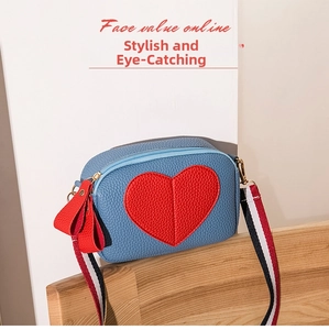 Detail of blue lychee texture crossbody bag with red heart stitching and striped strap