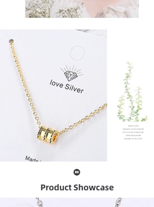 Detailed view of golden cylinder pendant necklace with black rivet accents on a white card