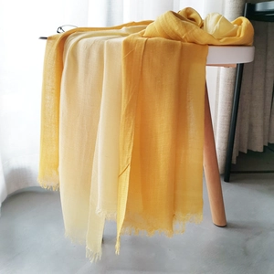 Detail view of a yellow gradient linen scarf with fringes on a wooden table