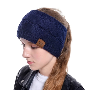Detail of dark blue cable knit headband with a brown leather MOK brand tag for winter