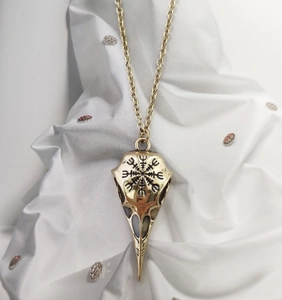 Detail of golden Viking crow skull necklace with Nordic engravings on white fabric