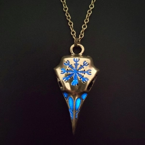 Macro detail of bronze viking crow skull necklace with glowing blue eyes in the dark