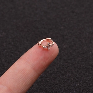 Close-up of a small rose gold cartilage earring with zircon cross on a fingertip