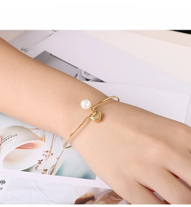 Elegant gold-plated open bangle featuring a heart charm and a white pearl on a wrist