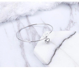 Macro detail of silver stainless steel open bangle with white pearl and heart charm